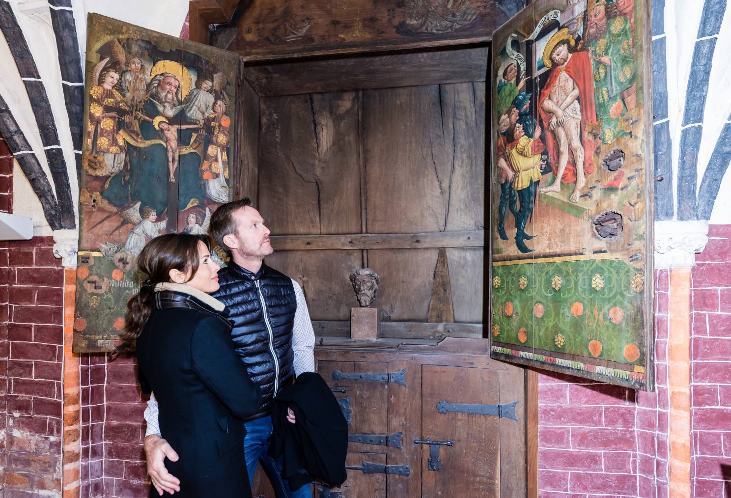 Paar steht Arm und im Arm in der Wunderblutkirche St. Nikolai in Bad Wilsnack und betrachtet lächelnd die mittelalterlichen Malereien der Wunderblutlegende an einer hölzernen Tür