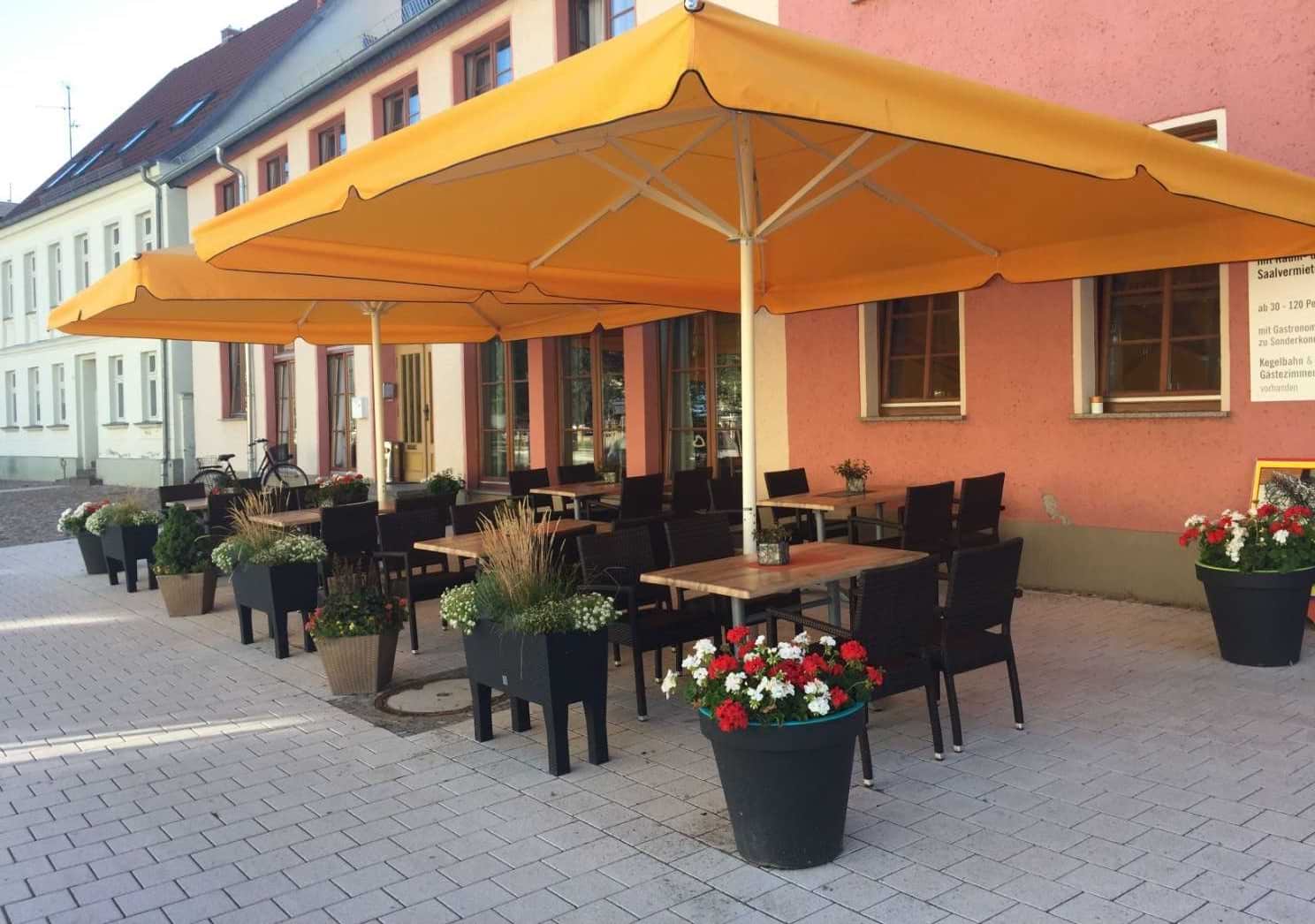 Terrasse mit Sitzmöglichkeiten, Blumen und aufgespannten Gastronomieschirmen