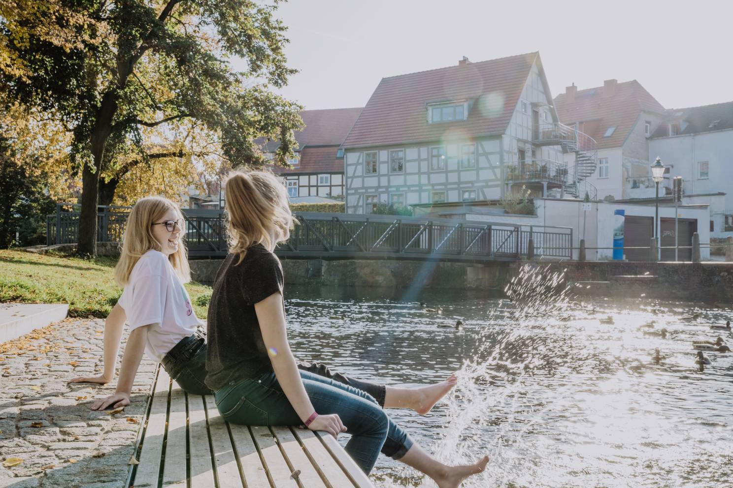 zwei junge Frauen sitzen am Wasser, Füße im Wasser, Brücke und Fachwerkhäuser im Hintergrund