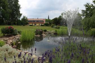 Vorschaubild Ein Teich mit Fontäne und Anpfalnzungen sowie eine weitläufige Wiese finden sich hinter dem Martinshof