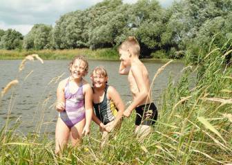 Vorschaubild drei Kinder in Badesachen stehen lachend im Schilf und zwischen Gräsern am Ufer des Badesees in Groß Woltersdorf 