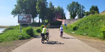 Vorschaubild zwei Radfahrerinnen auf der Grenzlandtour, E-Bikes und Helme, geplasterter Weg führt Bergauf