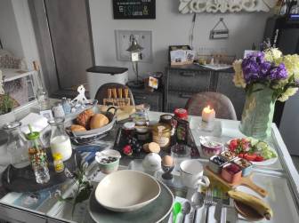 Vorschaubild reichlich gefüllter Frühstückstisch im Hotel La Maison Bett & Bike zur Übernachtung mit Obstteller, Gemüseteller, Käseplatte, Honigplatte, Marmelade, Eiern und Milch sowie frischen Blumen und Kerze in der Prignitz (Brandenburg)