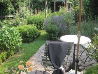Vorschaubild Zum Tag der Offenen Gärten öffnet der Garten der Familie Anschau mit Terrasse mit zwei Stühlen und Tisch unter einem Sonnenschirm neben vielfältiger Bepflanzung