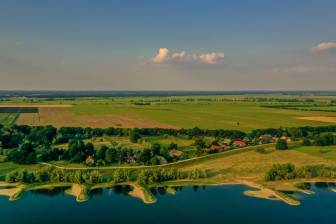 Vorschaubild Drohnenaufnahme von der Elbe mit ihren Buhnen und der dörflichen Idylle sowie der weiten Prignitzer Landschaft mit ihren Wiesen und Feldern hinter dem Elbdeich im Sommer