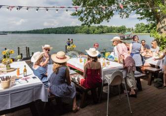 Vorschaubild Zahlreiche Gäste unterhalten sich auf Sitzbänken und an Tischen in dem Café und Restaurant INSL auf der Insel im Untersee zwischen Bantikow und Kyritz mit Blick auf das Wasser, den Steg mit badenden Kindern sowie die Fähre