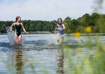 Vorschaubild zwei Mädchen in Badeanzügen rennen lachend durch den Untersee in Kyritz bei strahlendem Sonnenschein, sodass das Wasser nur so spritzt