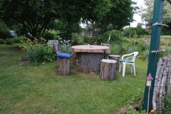 Vorschaubild Zum Tag der Offenen Gärten öffnet der Garten der Familie Gwozdz mit Holzstämmen als Stühlen und Tisch auf einer gemähten Wiese neben einer bunten Bepflanzung
