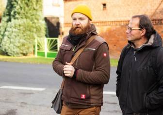 Vorschaubild Natur- und Landschaftsführer Robert Sommerfeld im Gespräch mit einem Gast an einer Straße, Mann mit Funktionssachen, gelber Mütze und rotem vollem Bart