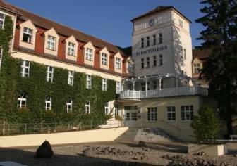 Vorschaubild von Efeu bewachsenes und mit einem Steingarten verziertes Kurmittelhaus in Bad Wilsnack im Sommer