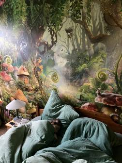 Vorschaubild schlafendes Kind unter Bettdecken im Schlafzimmer der Ferienwohnung Alpakahof in Rambow (Plattenburg, Prignitz) mit Blick auf die bemalte Dschungelwand hinter dem Bett mit Wechselschalter und Nachttisch