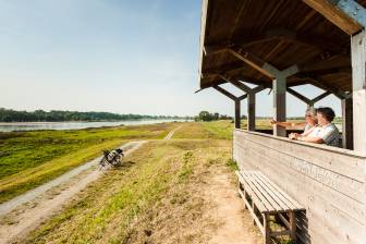 Vorschaubild zwei Fahrradfahrer rasten am Haltepunkt Natur und Aussichtspunkt Auenblick an der Deichrückverlegung und sehen sich den Elbdeich samt Elberadweg und dem Fluss Elbe im Biosphärenreservat Flusslandschaft Elbe an