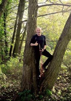 Vorschaubild Natur- und Landschaftsführer Olaf Wolff steht in einem Wald mit Nordic Waling Stöcken, lächelnder Mann mit Glatze und Bart in schwarzer Funktionskleidung