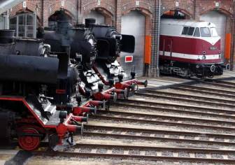 Vorschaubild Historischer Lokschuppen von Wittenberge mit mehreren Dampflokomotiven und einer historischen Bahn in den Garagenausfahrten und auf den Schienen