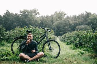 Vorschaubild Hipster-Fahrradfahrer macht eine Pause auf dem Beerenfeld und nascht im Regen