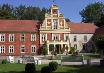 Vorschaubild Blick vom Park Meyenburg mit Buchsbäumen und weiß getünchten Bänken und Papierkörben auf das historische Schloss Meyenburg, in dem sich das Modemuseum und das Heimatmuseum befinden